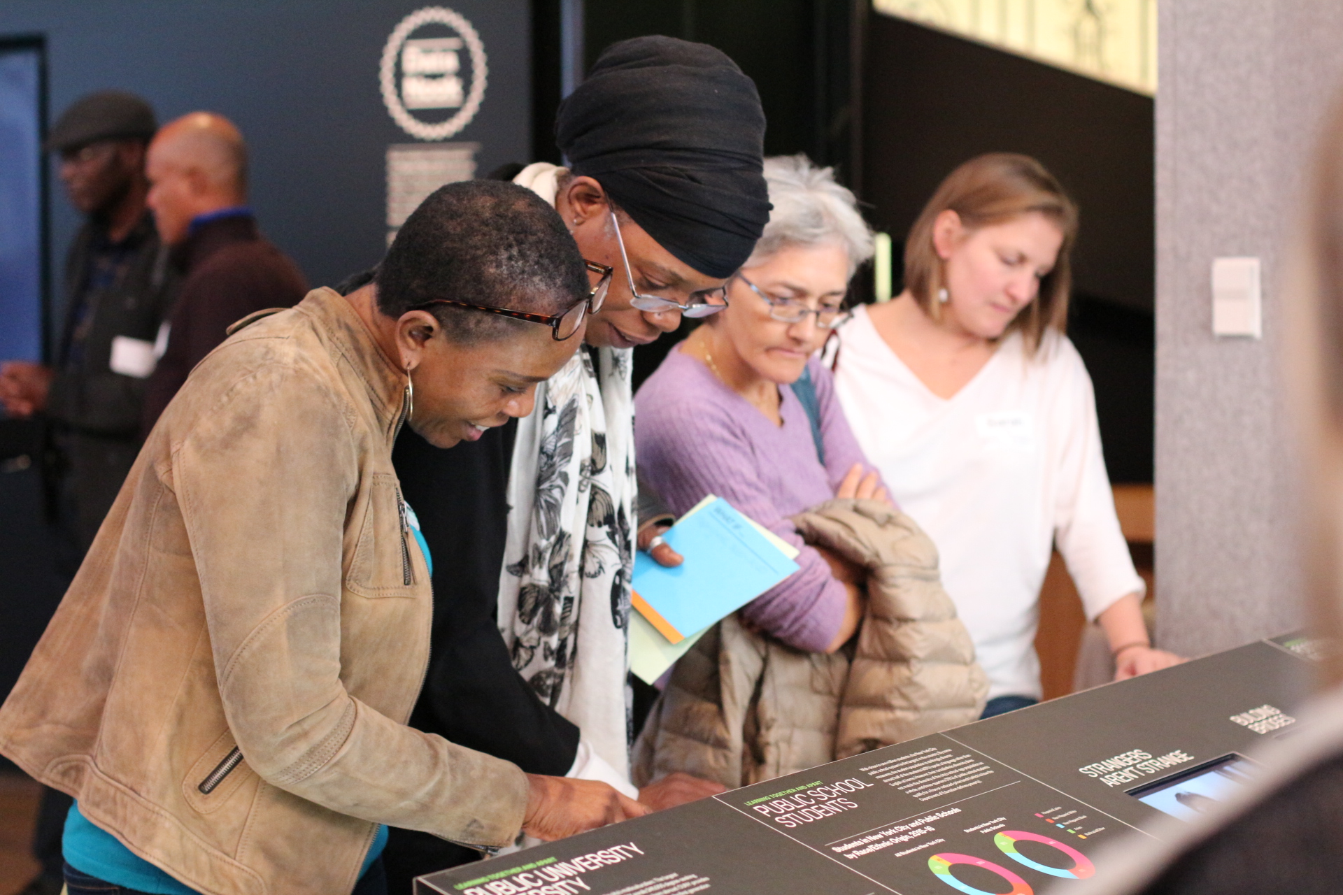 Four women observe a display in a gallery. 